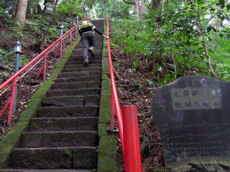 わきに石碑が建つ急な石段を登っていく
